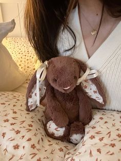 a woman holding a brown teddy bear on top of a bed next to a pillow