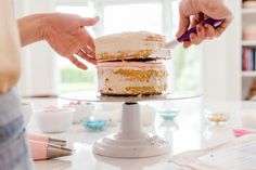 two people are decorating a cake with white frosting and gold decorations on it