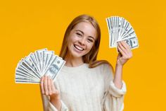 a beautiful young woman holding money in one hand and looking at the camera with an excited look on her face