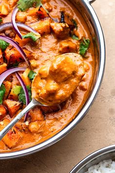 a bowl filled with chicken and vegetables on top of rice next to a silver spoon