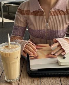 a woman sitting at a table with a book and a drink in front of her