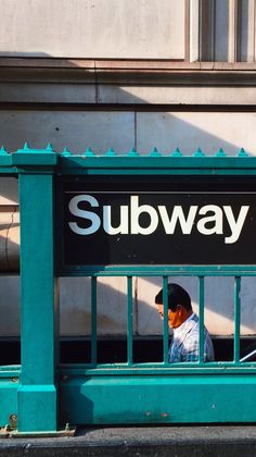 a man sitting on a bench in front of a subway sign with the word subway painted on it