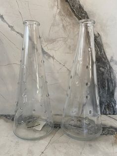 two clear glass vases sitting on top of a marble counter next to each other