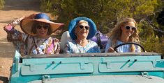 three women are riding in the back of an old blue truck and one is wearing sun glasses