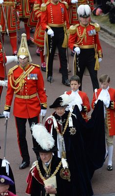 a group of men in red uniforms marching down the street with people dressed in costume