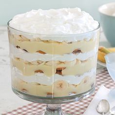 a layered cake with bananas and whipped cream in a glass dish on a checkered tablecloth