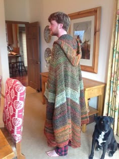 a man standing in a living room next to a black dog on the carpeted floor