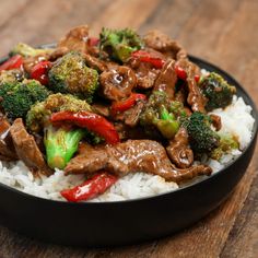 beef and broccoli stir fry over rice in a black bowl on a wooden table