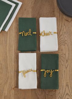 four napkins with gold lettering on them sitting on a wooden table next to other napkins