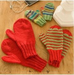 three knit mittens and gloves sitting on a table next to a laptop computer, mouse and headphones