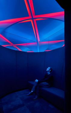 a man sitting on top of a blue couch under a red and blue sky light