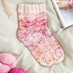 a pair of pink socks sitting on top of a bed next to yarn