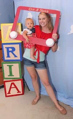 a woman holding a baby in her arms and standing next to blocks with letters on them