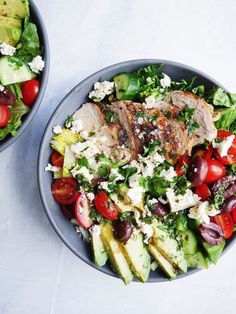 two bowls filled with salad and meat on top of a white tablecloth next to each other