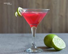 a red drink in a martini glass next to a lime