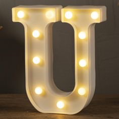 the letter u is lit up with light bulbs and sits on top of a wooden table