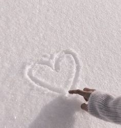 a person's hand is touching the snow with a heart drawn on it