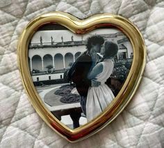 a gold heart shaped photo frame with a couple kissing in front of a white building