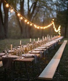 a long table is set with candles and place settings for an outdoor dinner in the woods