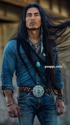 a man with long black hair wearing a blue shirt and cowboy hat is standing in front of a building