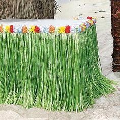 a table with grass and flowers on it in the sand near some palm tree trunks