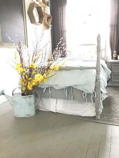 a white bed sitting in a bedroom next to a wooden table with flowers on it