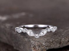 a white gold wedding band with three diamonds on top of it, sitting on a rock