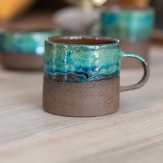 two coffee mugs sitting on top of a wooden table with blue and brown glaze