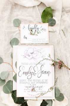 wedding stationery with flowers and greenery laid out on top of a white sheet