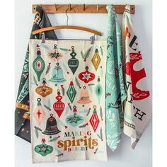 three tea towels hanging on a clothes rack with wooden hangers and colorful christmas ornaments