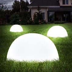 three white lights sitting on top of green grass in front of a house at night