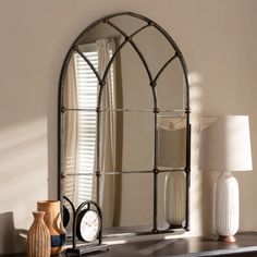 an arched mirror sitting on top of a dresser next to a lamp and vases