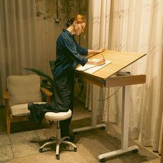 a woman sitting at a desk writing on a piece of paper in front of a chair