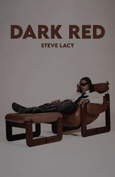 a man sitting on top of a brown chair next to a white wall with the words dark red