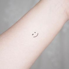 a small smiley face tattoo on the wrist is shown in black ink, and it appears to be smiling