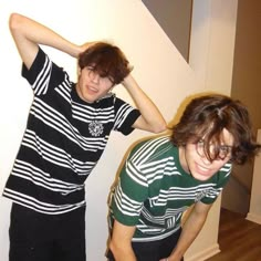 two young men standing next to each other in front of a white wall and wooden floor