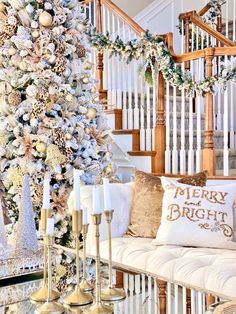 a white christmas tree with gold and silver ornaments on it next to a stair case