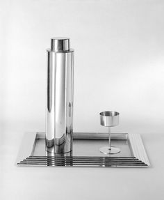 a silver candle holder sitting on top of a metal tray next to a glass cup