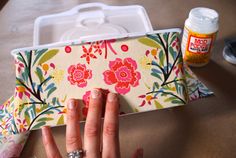 a woman's hand is holding onto a flowered case with scissors and glue on it