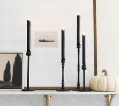 three candles are sitting on a mantle with two pumpkins