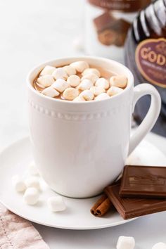 hot chocolate and marshmallows in a white cup on a saucer next to a bottle of booze