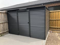 a large metal garage with sliding doors on the side and a wooden fence behind it