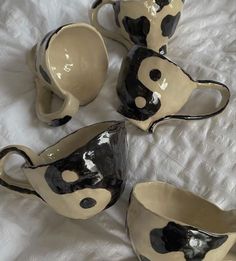 four black and white ceramic cups sitting on top of a bed