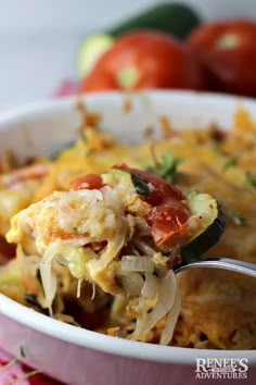 a spoon full of food with tomatoes and other vegetables in the background, on top of a bowl