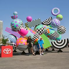 two people standing in front of a large sculpture with many balls and shapes on it