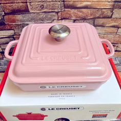 a pink casserole sitting on top of a white box with a red handle