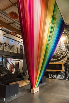 a large multicolored curtain hanging from the ceiling in an office building with black couches