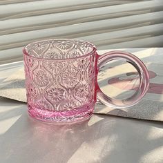 a pink glass cup sitting on top of a table next to a window sill