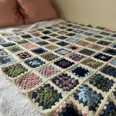 a crocheted blanket on top of a bed next to pillows and pillow cases