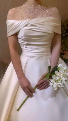 a woman in a white wedding dress holding a flower and wearing a tiara with pearls on it